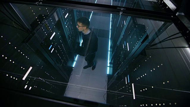 在满是主机架服务器的数据中心中，IT工程师使用笔记本电脑工作的俯视图。视频素材