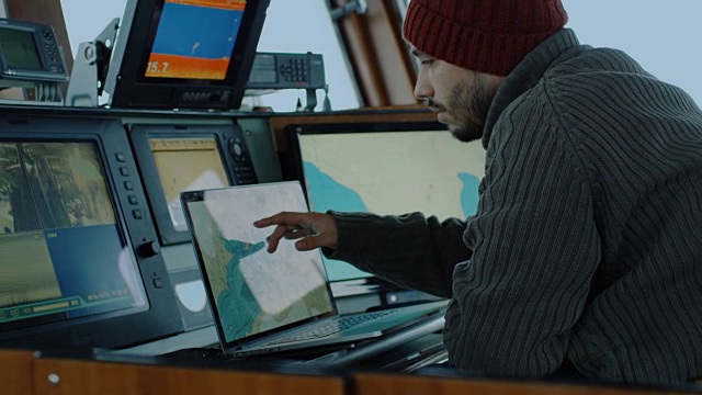 商业渔船的船长被监视器和屏幕包围着，在他的船舱里处理海图。视频素材