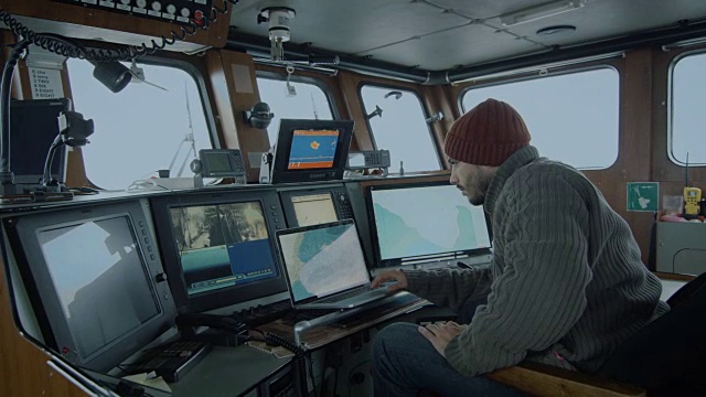 商业渔船的船长被监视器和屏幕包围着，在他的船舱里处理海图。视频下载