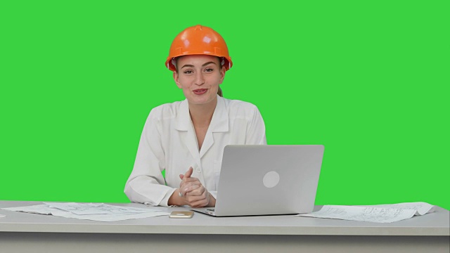 女工程师微笑着对着摄像机说话坐在桌子上有很多纸，绿色屏幕，Chroma Key视频素材