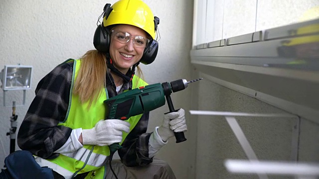 年轻的女建筑工人正在用钻头钻混凝土墙，并对着镜头微笑视频素材