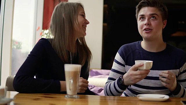 一对年轻夫妇坐在咖啡馆里。男人在喝茶，女人拿着一杯咖啡。4 k。视频素材
