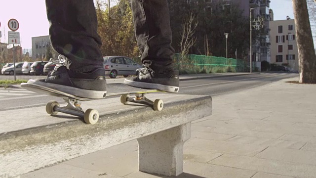 慢镜头特写:滑冰运动员跳跃和骑在城市街道的混凝土长凳上视频下载
