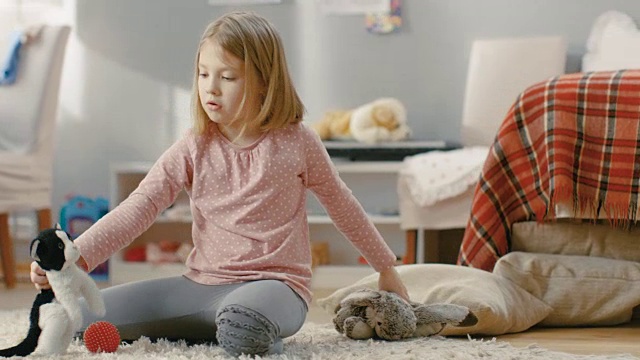 可爱的小女孩坐在地毯上玩毛绒玩具在她的灯光和舒适的房间。视频下载