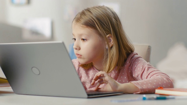可爱的年轻女孩坐在她的灯光房间的桌子旁使用笔记本电脑。视频素材