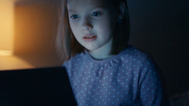 可爱的小女孩晚上在床上坐着平板电脑。视频素材