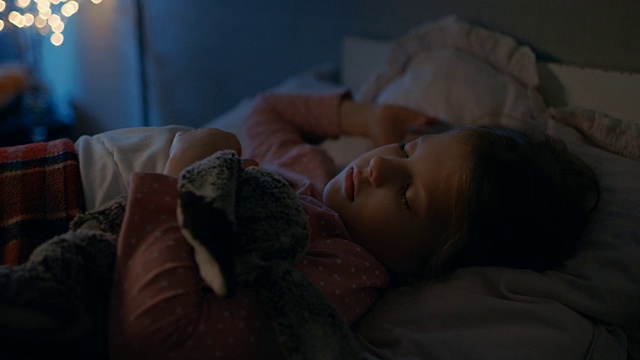 甜美的小女孩睡在她的床上，拥抱她的毛绒玩具。视频素材