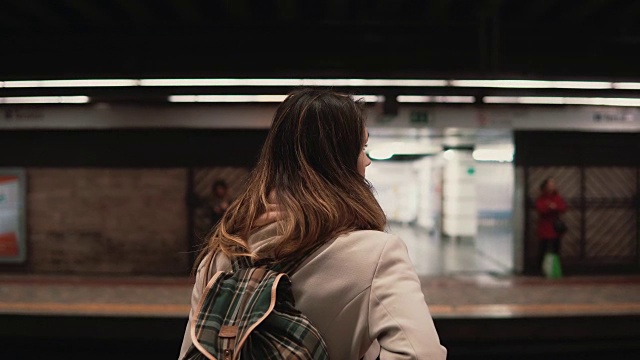 黑发女人站在火车站等待她的火车。晚上在地铁里的女孩看快速电车视频素材