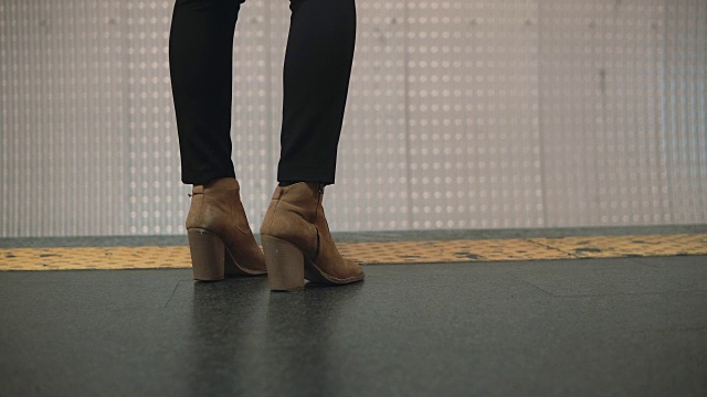 地铁站台上女人脚穿鞋的特写。女孩站在限制性的队伍旁边等待火车视频素材