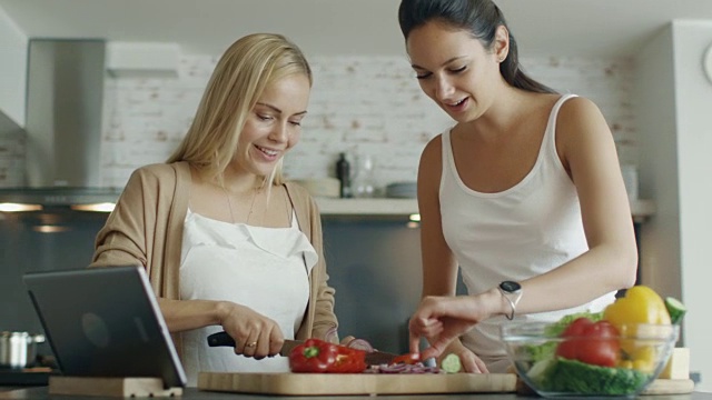 两个小女孩在厨房里做沙拉。他们还使用平板电脑搜索食谱视频素材