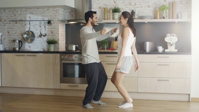 快乐的年轻夫妇在厨房跳舞，最后以拥抱结束。视频素材