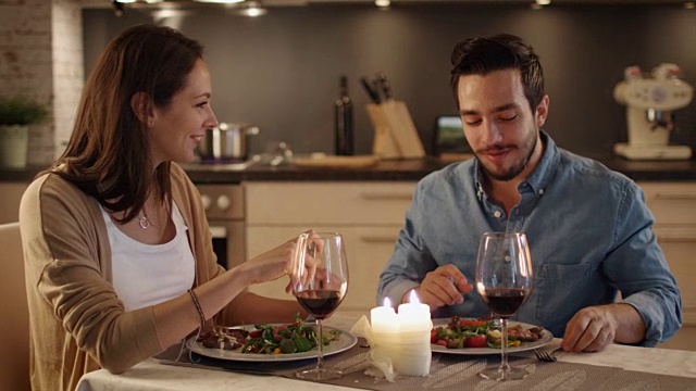 一对美丽的夫妇在厨房里吃烛光晚餐。他们吃喝聊天。两个都有好心情和微笑很多。缓慢的运动。视频素材