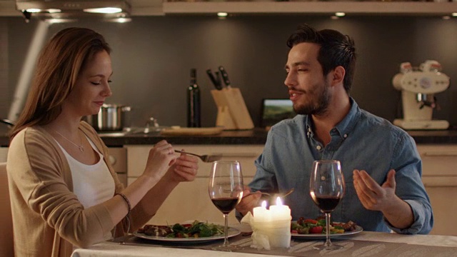 一对美丽的夫妇在厨房里吃烛光晚餐。他们吃喝聊天。两个都有好心情和微笑很多。结束运动。视频素材