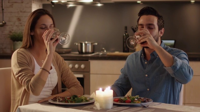 一对美丽的夫妇在厨房里吃烛光晚餐。他们吃喝聊天。庆祝时他们碰杯。视频素材
