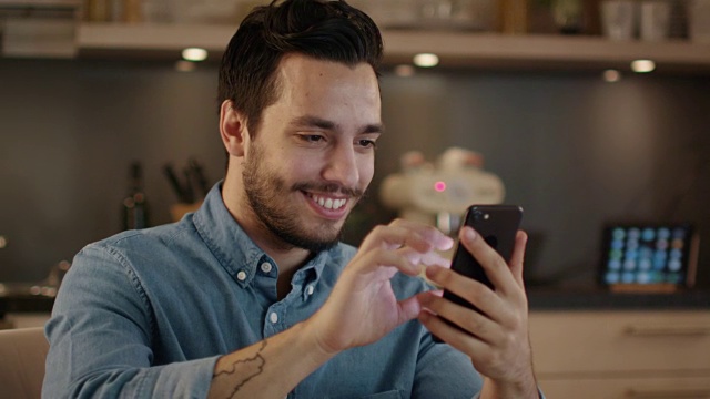 英俊的年轻人微笑着在厨房使用智能手机。视频素材