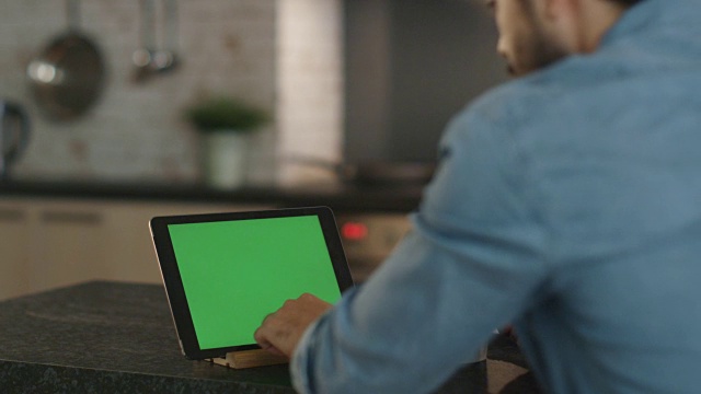 在厨房里。一名年轻人一边用绿色屏幕的平板电脑一边喝着杯子里的水。视频素材