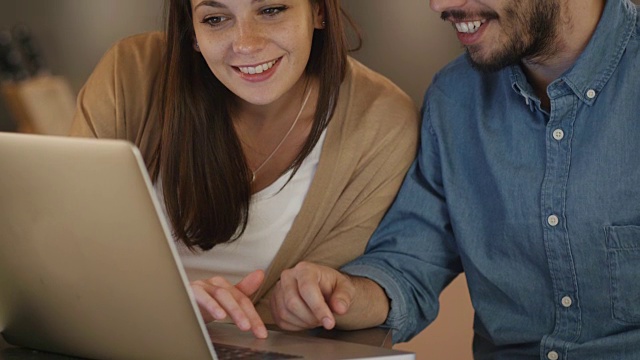 年轻夫妇坐在笔记本电脑前聊天。帅哥给女友看屏幕上的东西。视频素材