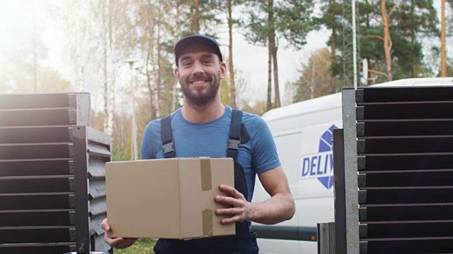 微笑的快递员从他的货车里出来，带着纸板箱，走向相机。视频素材