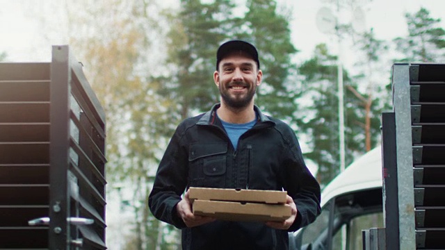 微笑的披萨外卖员送了两个披萨。阳光明媚的秋天，背景是黄桦树和松树。视频素材