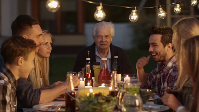一群人围坐在一张桌子上，在家庭晚餐期间吃，交流和玩。视频下载
