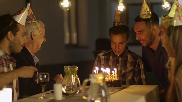 快乐微笑的男孩吹灭她生日蛋糕上的蜡烛。男孩被他的家人和朋友包围着视频素材