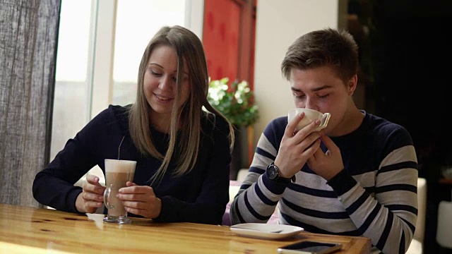 一对年轻夫妇坐在咖啡馆里。男人在喝茶，女人拿着一杯咖啡。4 k。视频素材