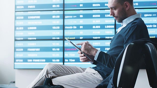 一名男子在机场候机室等候登机时使用平板电脑。视频下载