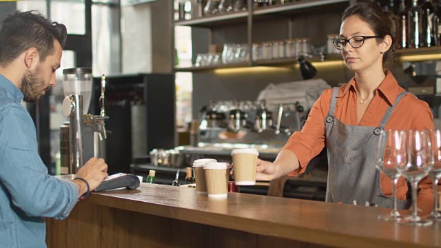 一个帅气的年轻人在咖啡店用信用卡为外卖咖啡买单。视频素材