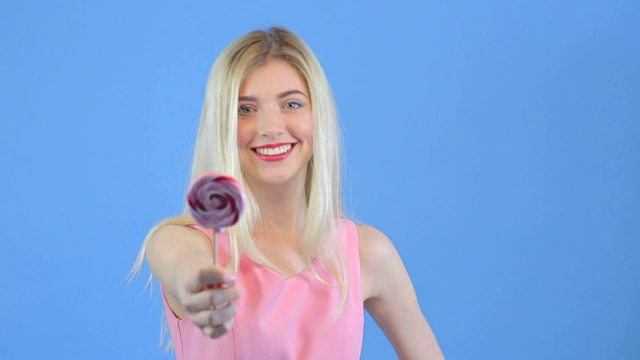 年轻女子给颜色闪亮的棒棒糖，在蓝色的背景视频素材