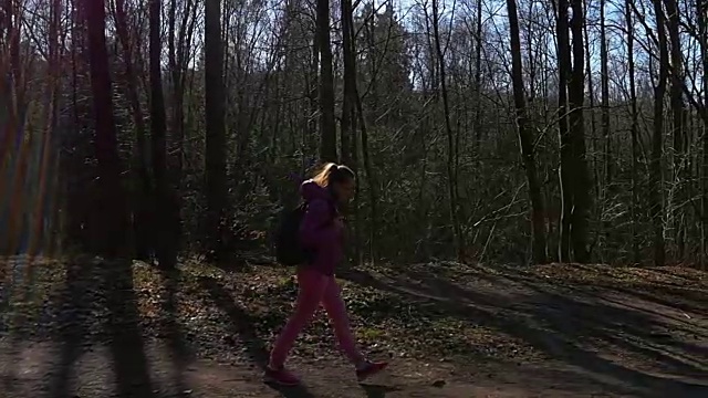 美丽的年轻女孩走在森林里。背景黑暗的树在阳光。粉红色的衣服，春天的森林，慢镜头视频素材
