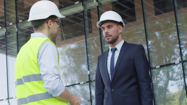 戴安全帽的商人和工程师在建筑工地握手。视频素材