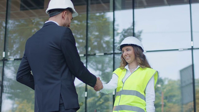 戴安全帽的商人和女工程师在建筑工地握手。视频素材