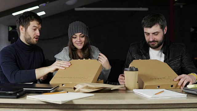 一组年轻的创意工作者打开装有披萨的纸盒，感到惊喜和快乐。送比萨饼到办公室。Slowmotion视频素材