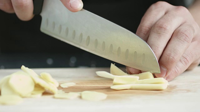 厨师长正面用刀将生姜切成薄片，放在砧板上。视频素材