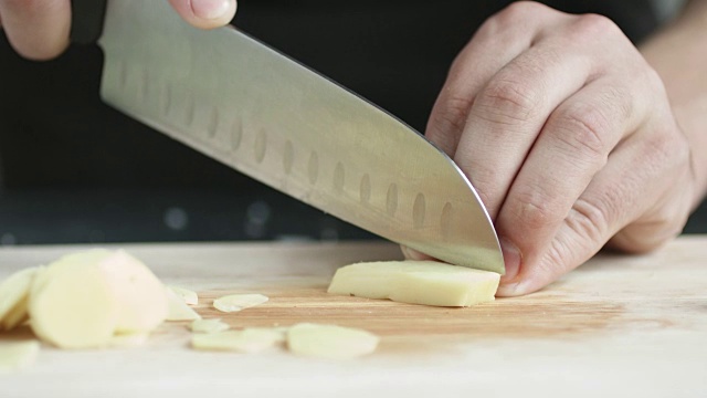 厨师长正面用刀将生姜切成薄片，放在砧板上。视频素材