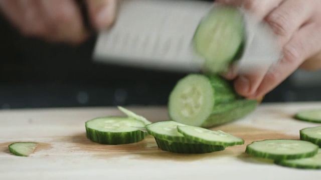 年轻厨师用刀在切菜板上切出绿色有机黄瓜薄片。视频素材