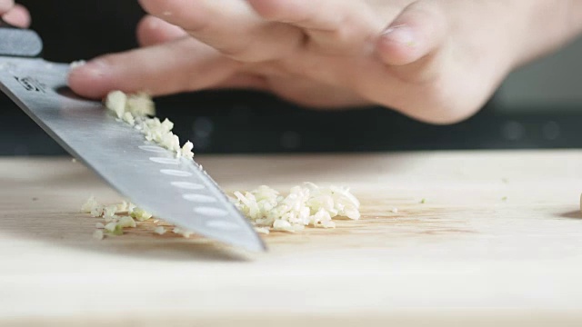 正前方的厨子用刀把大蒜切成薄片放在切菜板上。视频素材