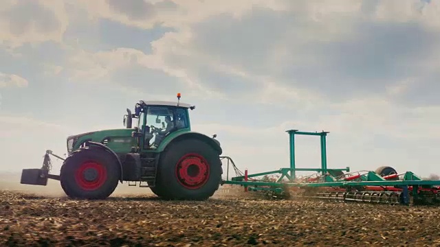 跟踪镜头:拖拉机在田里犁地。春天的野外工作。天气好，阳光明媚。低角度3轴稳定视频视频素材