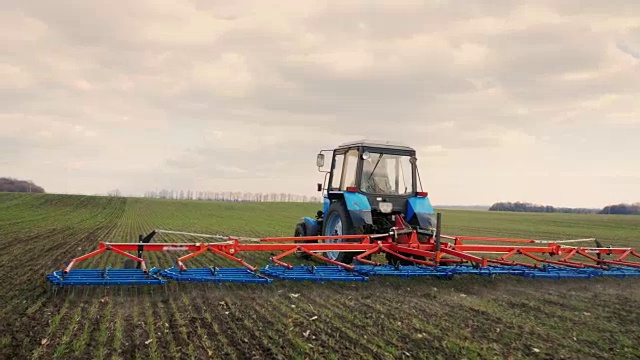 斯坦尼康镜头:拖拉机向前，用一台耕耘机耕耘土地。春天的野外工作视频下载
