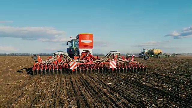 斯坦尼康镜头:在早春的时候，两台拖拉机和播种机在地里播种小麦。后视图视频素材