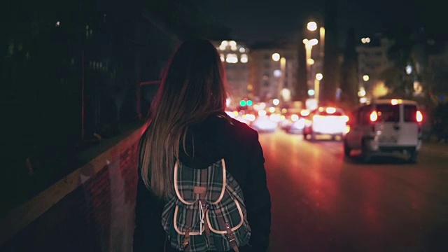 后视图的深色头发的女人在交通时间走在道路附近。女孩深夜独自穿过城市视频素材