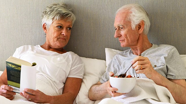 老人在吃早餐，而女人在床上看书视频素材