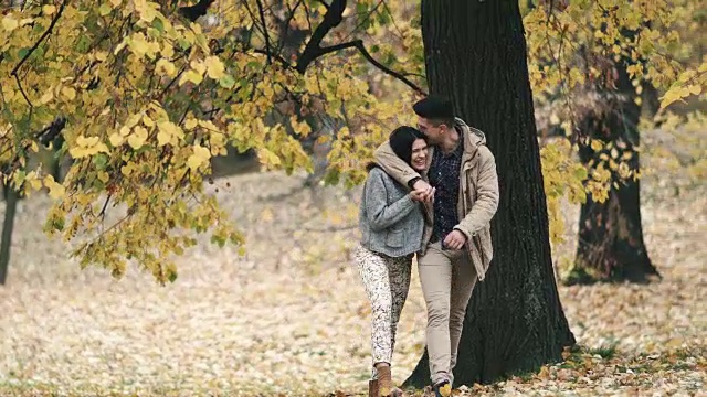 秋日公园里，一对快乐的年轻情侣在散步时拥抱在一起。视频素材