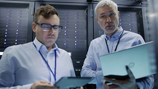 从机架服务器机柜拍摄的视频。两名IT技术人员使用笔记本电脑和平板电脑工作的硬件和软件。视频素材