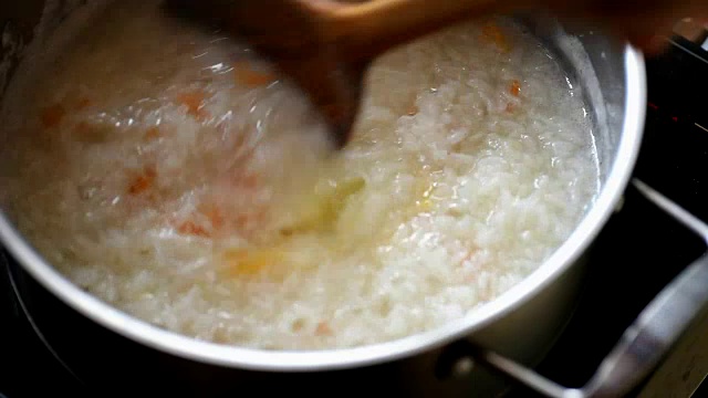 在不锈钢锅中加入开水，用木勺将米饭混合视频素材