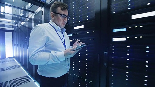 以下是IT工程师与一排排机架服务器穿过数据中心走廊的照片。他使用平板电脑。视频素材