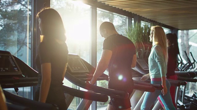 年轻的运动员一边使用智能手机一边锻炼，在健身房的跑步机上跑步。视频素材