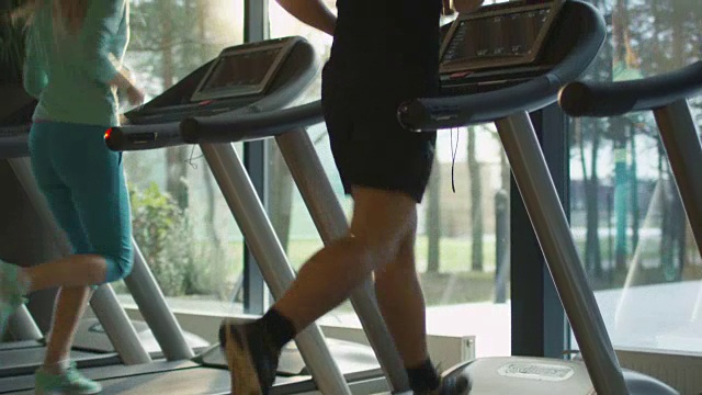年轻的男女运动员在运动馆里的跑步机上锻炼和跑步。视频素材