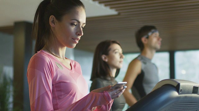 适合运动的白人女孩正在跑步机上运动健身房与耳机和电话。视频素材