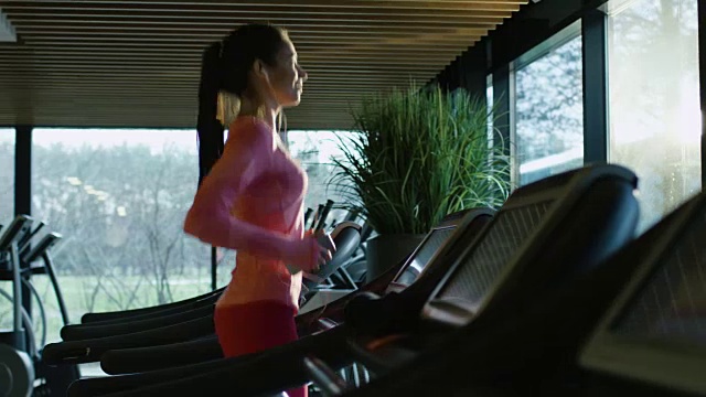 有吸引力的白人女孩开始在跑步机上跑步在一个空的体育健身房戴着耳机。视频素材